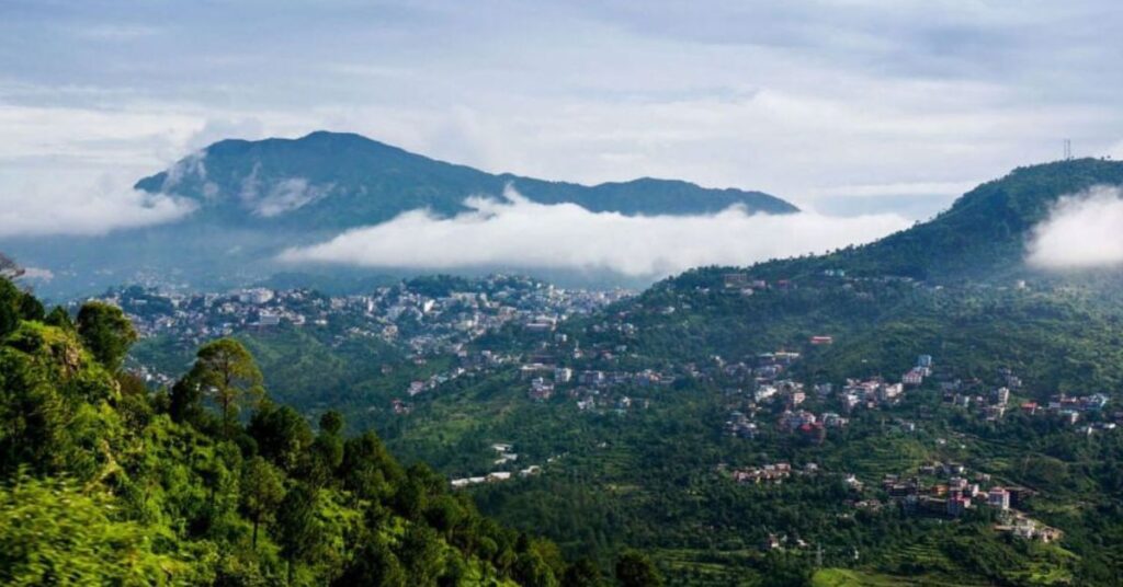 Scenic view of Mussoorie during the monsoon season with mist-covered hills, lush greenery, and rain-soaked roads