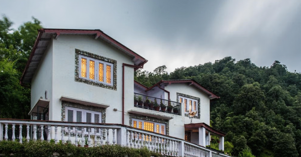 A cozy wooden homestay cottage with a balcony overlooking lush green hills and pine trees near Nainital, perfect for a peaceful mountain stay.