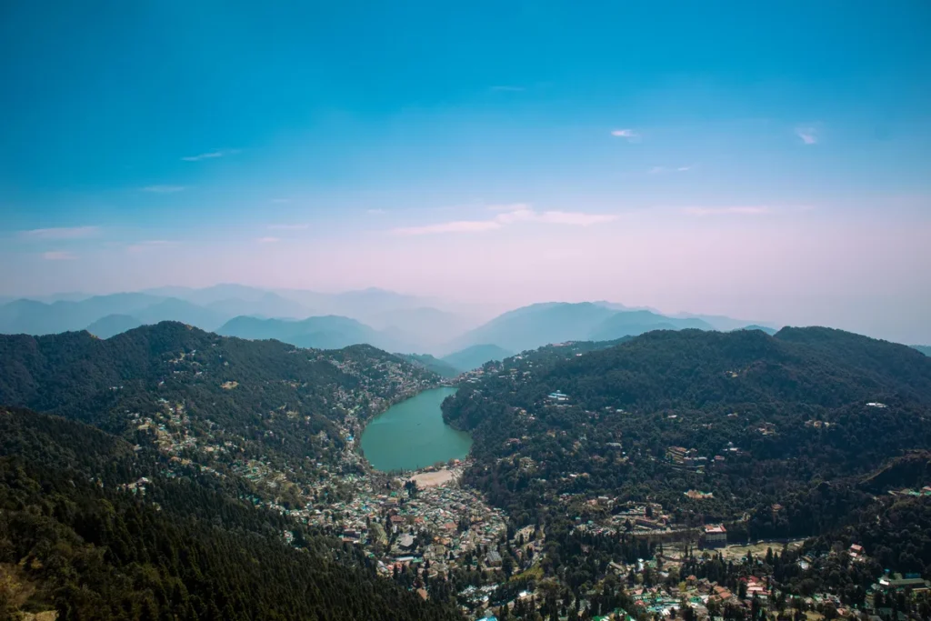 A panoramic view of Nainital in summer, showing Naini Lake surrounded by green hills and a clear blue sky — the perfect cool retreat from India’s summer heat.