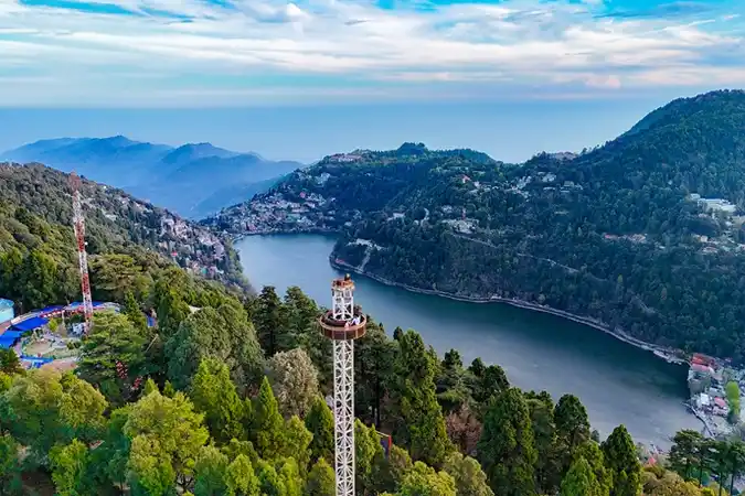 Aerial view of Nainital town and Naini Lake surrounded by green hills and mountains in the background.