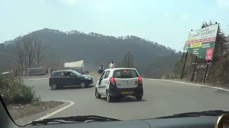 Car on highway passing through Kumaon region with hills visible