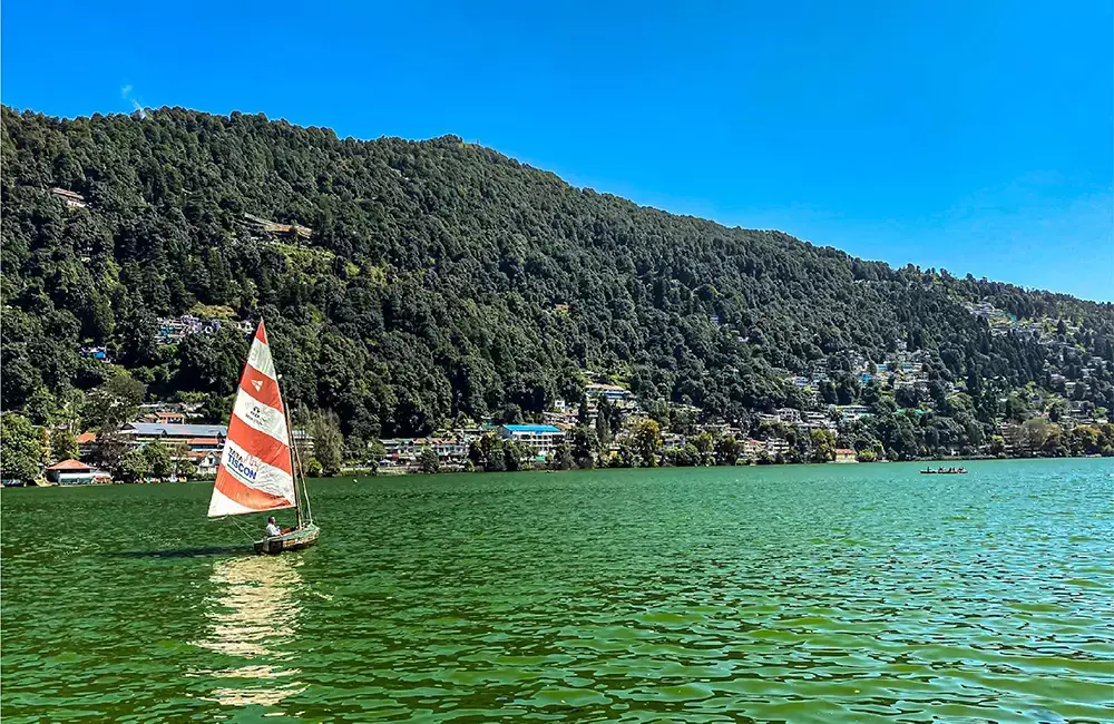Naini Lake in Nainital with colorful boats in the foreground and green hills in the background under a clear blue sky
