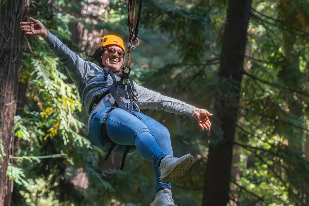 Tourist enjoying bungee jumping in Nainital, suspended in mid-air with safety harness and helmet amid lush forest surroundings.