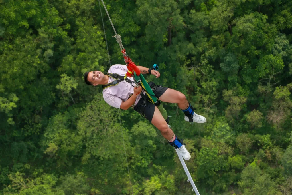 Bungee jumping in Nainital with a smiling torist suspended by safety harness over a dense green forest valley.