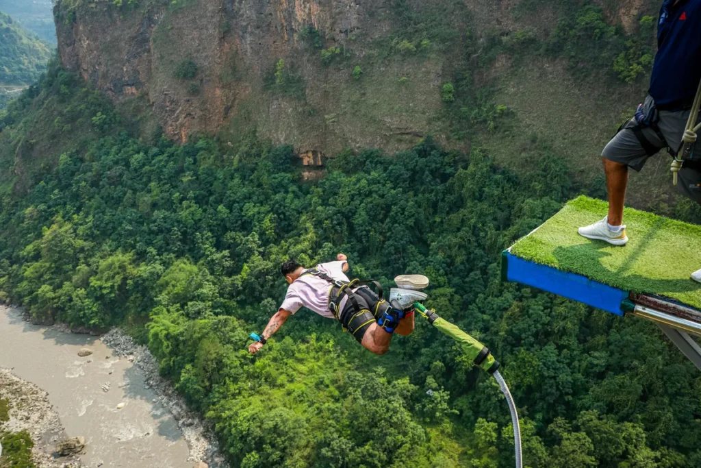 Person performing bungee jumping in Nainital from a platform over a deep green valley and river, showcasing an extreme adventure experience.