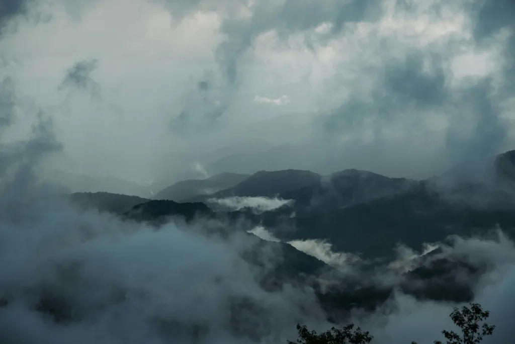 Misty winter morning view of Nainital’s mountain ranges covered in dense clouds and fog, creating a serene and mysterious atmosphere with layers of hills fading into the distance.