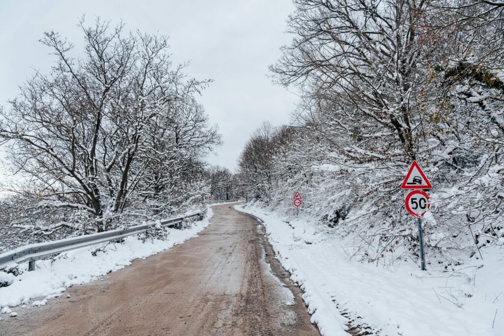 Snow-covered mountain road with warning signs and frosted trees along the Delhi to Nainital route in January, capturing the beauty of winter travel.