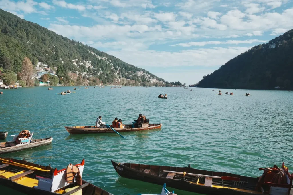 Tourists enjoying boat rides on Naini Lake in Nainital during summer, surrounded by lush green hills and clear blue skies — a perfect escape from the heat.