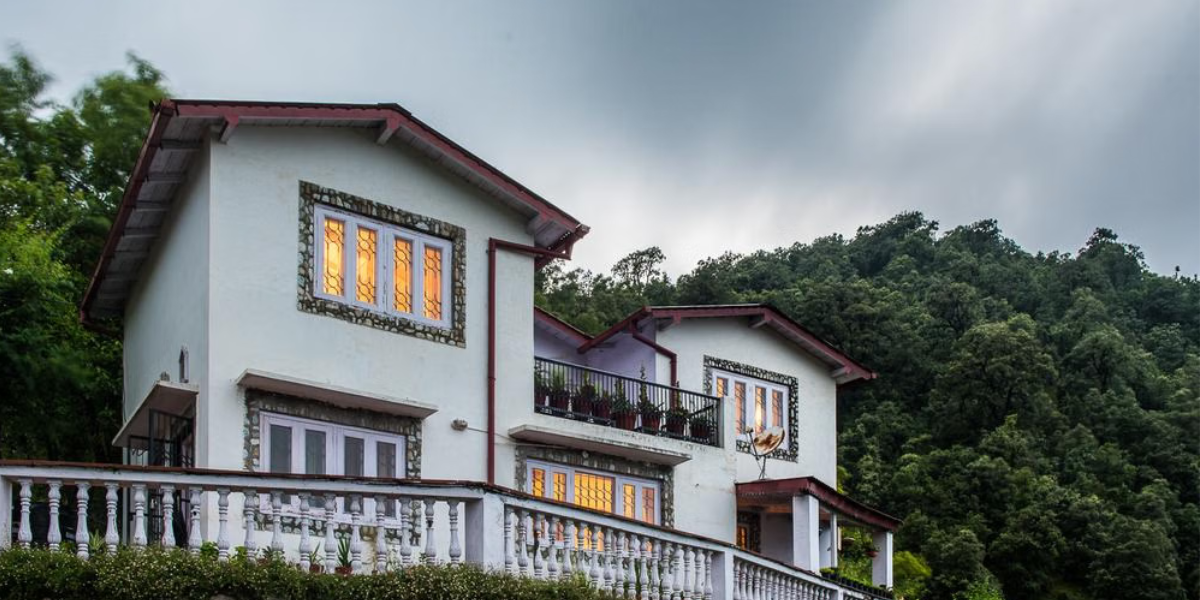 A cozy wooden homestay cottage with a balcony overlooking lush green hills and pine trees near Nainital, perfect for a peaceful mountain stay.