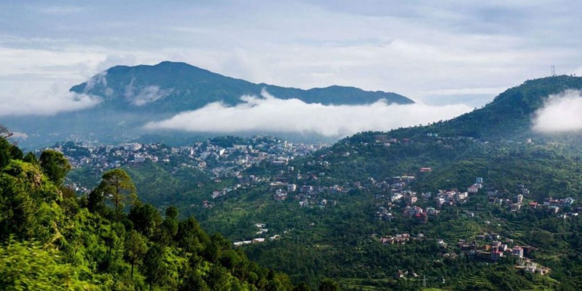 Scenic view of Mussoorie during the monsoon season with mist-covered hills, lush greenery, and rain-soaked roads