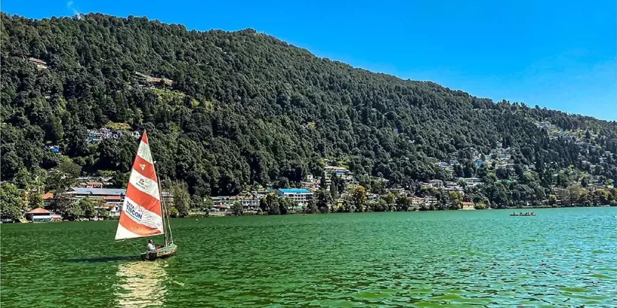 Naini Lake in Nainital with colorful boats in the foreground and green hills in the background under a clear blue sky