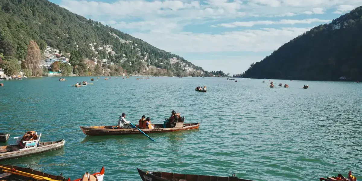 Boats floating on the calm turquoise waters of Nainital Lake surrounded by lush green hills under a bright blue sky.