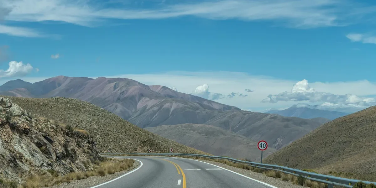 Scenic mountain road representing the Nainital Distance from Delhi route with clear blue skies and winding hills.